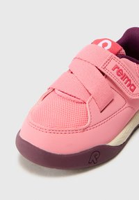 Roze sportska cipela s mrežastim gornjim dijelom, dvostrukim čičak trakama i hrapavim gumenim potplatom. Ima kontrastni ljubičasti potplat i logo.