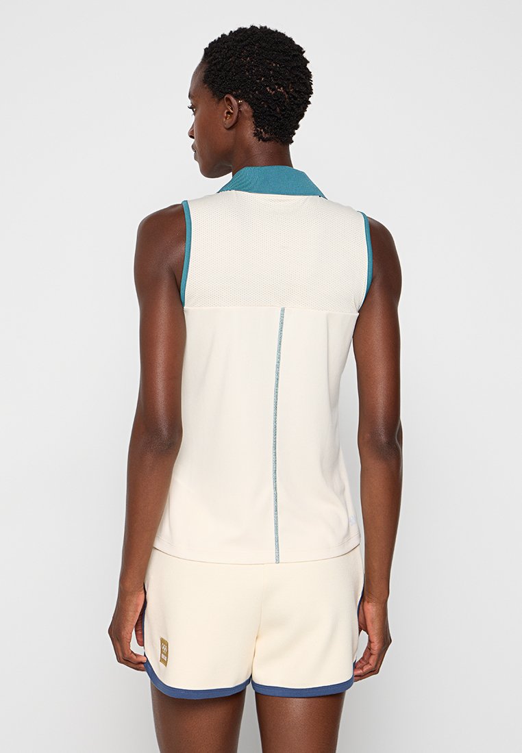 Ärmelloses hellcremefarbendes Oberteil mit einem Netzoberteil, tealfarbenem Kragen und kontrastierenden Nähten. Kombiniert mit cremefarbenden Shorts mit marineblauen Akzenten.
