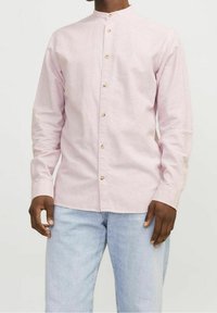 Camicia rosa chiaro a maniche lunghe con colletto alla coreana e chiusura con bottoni. Presenta bottoni in legno e un tessuto liscio e strutturato.