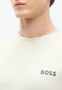 Ανοιχτό μπεζ κοντομάνικο T-shirt από λείο ύφασμα με στρογγυλή λαιμόκοψη. Διαθέτει σκουρόγκρι λογότυπο "BOSS" στο στήθος.