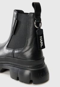 Zwarte leren enkelboots met elastische zijpanelen, dikke rubberen zool, gestructureerde accenten en een merklabel aan de achterkant.