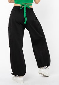 Schwarze, locker sitzende Cargo-Hosen mit elastischem Bund und grünem Kordelzug, ausgestattet mit Seitentaschen und Kordelzugbündchen.