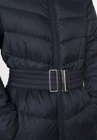 Marineblaue Steppjacke mit gestepptem Muster, ausgestattet mit Reißverschluss und breitem Taillengürtel, akzentuiert durch eine silberne Metallschnalle.