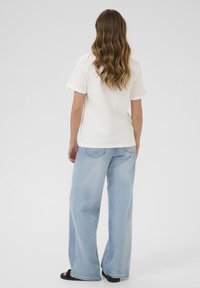 Cream short-sleeve shirt with rolled cuffs, paired with light blue wide-leg jeans. The outfit features a relaxed fit and casual fabric textures.