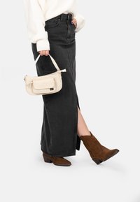 Gonna di jeans nera con spacco laterale, borsa crema e stivaletti in suede marrone con cuciture decorative. Pullover bianco accogliente.