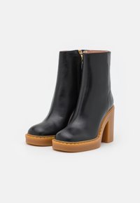 Botines de cuero negro con puntera redonda, plataforma gruesa color marrón claro y tacón alto de bloque. Cuenta con cremallera lateral y suela texturizada.