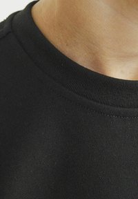 Svart t-shirt med rund halsringning som har ribbat halsband och slät textur. Närbild av tygdetaljer som framhäver sömmar och passform.