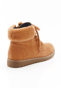 Bruine suede enkellaars met een bontkraag, vetersluiting aan de voorkant en een gestructureerde rubberen zool, weergegeven vanuit een zijaanzicht op een witte achtergrond.