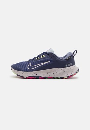 Chaussure de sport bleu marine et grise avec semelle tachetée, accents néon, logo Nike sur le côté, col rembourré et languette au talon.