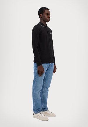Black long-sleeve polo shirt with white trim, logo on chest; paired with light blue denim jeans and beige sneakers. Simple, casual design.