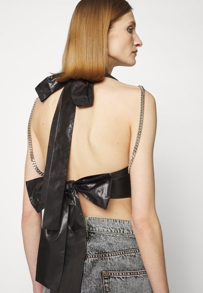 Black faux leather crop top with a large back bow, chain straps, and open back design. Features a smooth texture and clean lines.