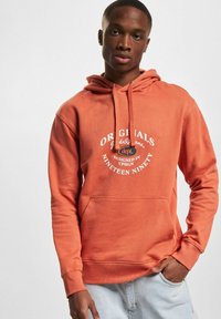 Orangene Baumwollkapuzenjacke mit einer Vordertasche, verstellbarem Kapuzenzug und weißem grafischem Text, der "ORIGINALS" und "DESIGNED IN CPHGN" liest.