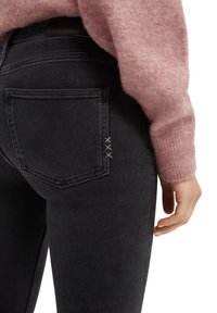 Vaqueros de mezclilla negros con un bolsillo trasero con costuras decorativas y un diseño ajustado, acompañados de un suéter de textura en rosa claro.