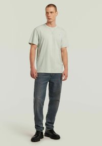 T-shirt di cotone verde chiaro con maniche corte, colletto rotondo e piccolo logo. Abbinata a jeans di denim scuro e scarpe chunky nere.