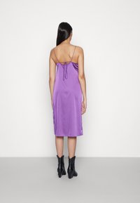 Vestido midi de cetim roxo com alças finas ajustáveis, apresentando um detalhe de cordão nas costas e uma textura suave e brilhante.