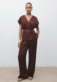 Top texturat burgund cu maneci late și talie legată, alăturat de pantaloni burgund largi, completat cu încălțăminte și accesorii în nuanțe neutre.