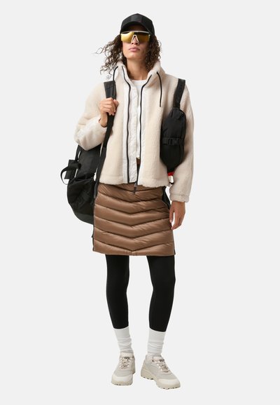 Fleecejakke, hvid skjorte, brun dunnederdel, sorte leggings, hvide sokker og beige sneakers. Guldsunglasses og en sort kasket. To rygsække.