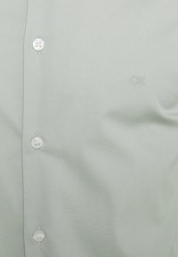 Camicia button-up verde chiaro con bottoni bianchi e piccolo logo ricamato "CK" sul petto.