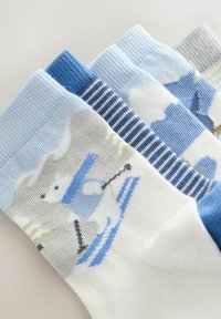 Tre par sokker: en hvid med en pingvin, der står på ski, en lyseblå med striber, og en grå med et blåt design. Materialet er en bomuldsblanding.