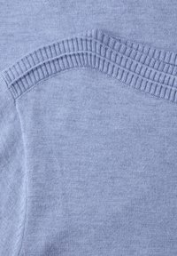 Tissu en maille bleu clair montrant un gros plan sur la couture côtelée de l'épaule d'un pull et le motif texturé en maille.