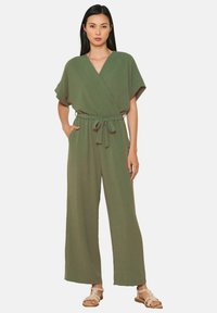 Mono verde oliva con diseño cruzado, mangas amplias y cinturón ajustado en la cintura. Fabricado en tejido suave con una silueta fluida.