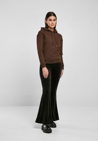 Sudadera marrón con capucha ajustable, combinada con pantalones de terciopelo negros acampanados y zapatos de plataforma negros gruesos. Diseño y texturas minimalistas.