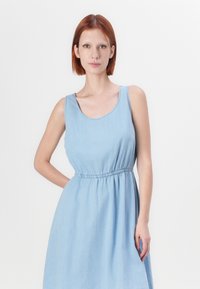 Svetlomodré denim šaty s bezrukávovým dizajnom a okrúhlym výstrihom. Obsahujú elastický pás a voľný sukňový strih po kolená.
