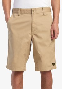 Beige shorts lavet af en bomuldsblandingsstof. Har flad front, sidelommer og et lille mærke nær den højre kant.
