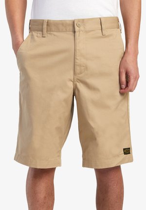 Beige shorts made of cotton blend fabric. Features a flat front, side pockets, and a small brand tag near the right hem.