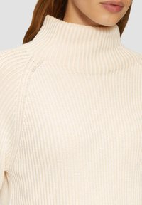Crème col roulé trui met ribbelstructuur, voorzien van een aansluitend ontwerp en zacht materiaal. Opvallende wijde kraag en naadloze schouderdetails.