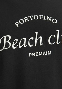 Čierna tkanina s bielym potlačeným textom: "PORTOFINO Beach club PREMIUM." Dizajn má zakrivený typografický štýl. Textúra vyzerá hladko.