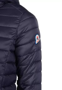 Giubbotto imbottito navy con cuciture orizzontali, caratterizzato da un patch con logo sulla manica. Il tessuto appare lucido e liscio.