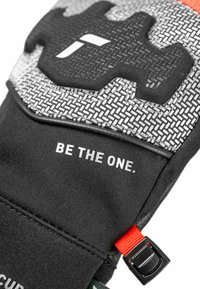 Schwarze und graue Handschuhe mit strukturierten Mustern, rotem Akzentband und dem aufgedruckten Text "BE THE ONE" auf einer glatten Oberfläche. Verfügt über ein Logodesign.