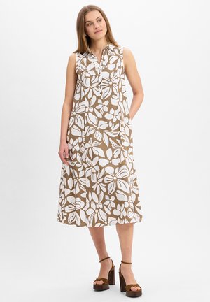 Beige sleeveless dress with a white floral pattern, button-down front, and side pockets. Worn with brown heeled sandals.