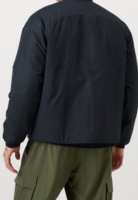 Giacca imbottita blu navy con colletto alto e polsini elasticizzati. Tessuto liscio, materiale leggero, con un discreto logo dettagliato sulla manica.