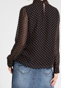 Black sheer long-sleeve blouse with orange polka dots paired with a blue denim skirt, showing back view of the outfit.