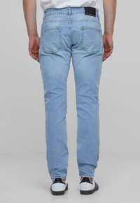 Jeans de mezclilla azul claro con un diseño de pierna recta, que cuentan con dos bolsillos traseros y costuras en contraste, combinados con zapatos en blanco y negro.