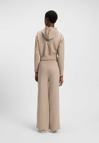 Felpa con cappuccio beige e pantaloni a gamba larga, realizzati in tessuto morbido, con polsini elasticizzati e una vestibilità rilassata. Design minimalista senza ulteriori motivi.