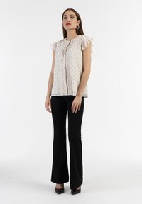 Blusa chiara a maniche corte con motivo floreale e volant, abbinata a pantaloni neri a campana aderenti e tacchi alti neri.
