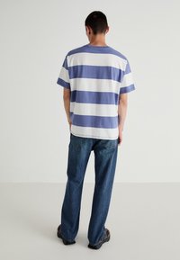 T-shirt riscada em azul claro e branco, mangas curtas, corte relaxado. Combinada com jeans de denim azul e calçado castanho. Textura plana.