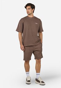 T-shirt marron à manches courtes et côtes avec logo brodé associé à un short assorti. Conçu avec une coupe décontractée et une texture douce.