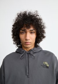 Γκρι φούτερ με κορδόνι στο λαιμό, με κεντημένο λογότυπο και λουλουδάτο σχέδιο. Μαλακό ύφασμα με χαλαρή εφαρμογή.