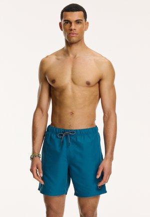 Pantaloni de baie teal, cu talie elastică și șnur. Material neted, lungime deasupra genunchiului, având un detaliu mic cu logo.