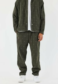 Chándal verde oliva con un sutil patrón de 'PXP', que incluye una chaqueta abotonada y pantalones con cintura elástica, combinados con zapatillas blancas.