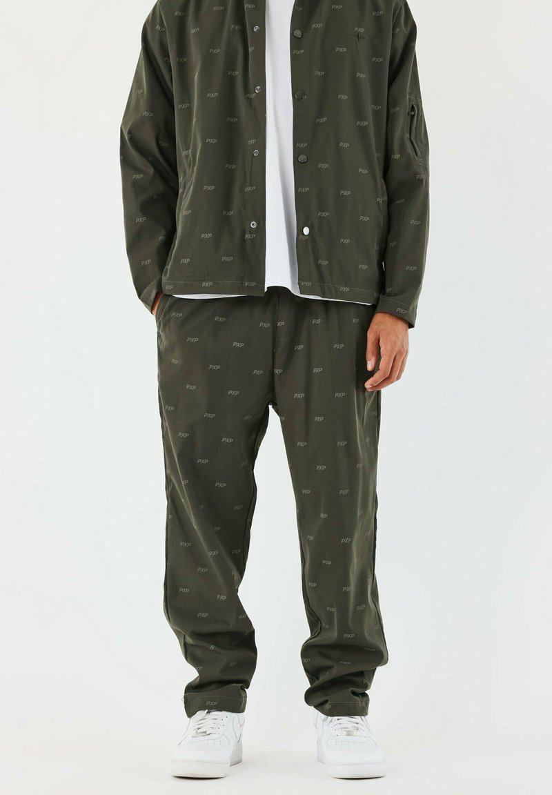 Chándal verde oliva con un sutil patrón de 'PXP', que incluye una chaqueta abotonada y pantalones con cintura elástica, combinados con zapatillas blancas.