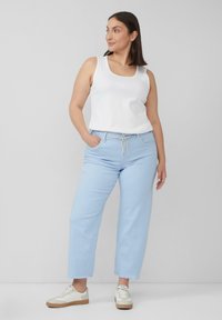 Jasnoniebieskie dżinsy w szerokim kroju z postrzepionymi brzegami, zestawione z białym topem na ramiączkach. Białe sneakersy z brązowymi akcentami dopełniają stylizację.