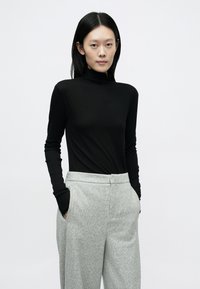 Sort rullekravebluse med lange ærmer, kombineret med lysegrå teksturerede højtaljede bukser med sidelommer og en afslappet pasform.