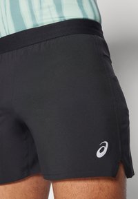 Black athletic shorts made of stretchy fabric, featuring a wide waistband and a small white logo on the left side.
