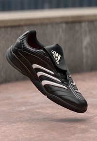 Scarpa atletica nera con upper sintetico testurizzato, tre strisce bianche, colletto imbottito e suola in gomma elevata. Design leggero.