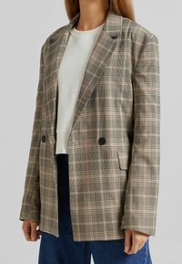 Marynarka w kratę w odcieniach beżu, czerni i różu. Posiada dopasowany krój, dwa guziki i kieszenie boczne. Nosi się na białej koszuli.